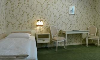 A simple bedroom with white wall decoration and a bed. A table and two chairs complement the space.