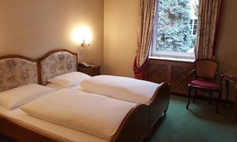 A cozy bedroom with two single beds and a large window. Next to the bed is a chair and a table.