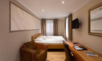 A modern room with a double bed, a desk, and an armchair. Large windows let in plenty of light and create an inviting atmosphere.