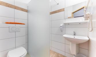 A modern bathroom with a shower, sink, and toilet. The walls are decorated with white tiles and a decorative border.
