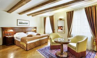 A cozy bedroom with a large bed and seating. Bright curtains let in plenty of light and create an inviting atmosphere.