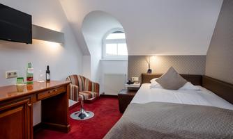 A modern hotel room with a large bed and a cozy seating area. There is a television on the wall and a wooden desk.