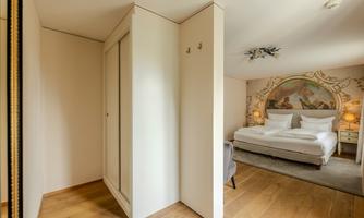 A modern bedroom with a large bed and a decorative wall mural. The room has light walls and a warm wooden floor.