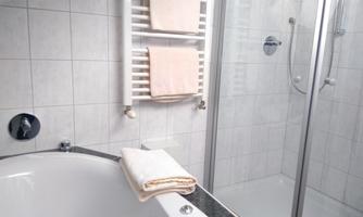 A modern bathroom with a bathtub and a shower cabin. The walls are tiled and towels are neatly hung.