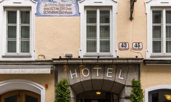 A charming hotel building with a colorful mural and large windows. Two green plants stand in front of the entrance.