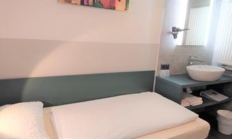 A simple, modern bedroom with a single bed and a sink. The room is bright and functionally furnished.