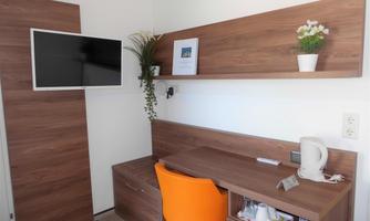 A modern room with a desk, a comfortable chair, and a television on the wall. On the shelf are plants and a decorative picture.