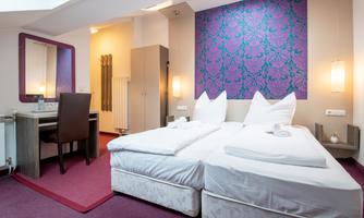 A stylish hotel room with two beds and a decorative headboard. The room features a desk and a large mirror.