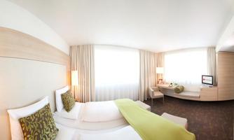 A modern hotel room with two single beds and a bright, inviting atmosphere. Large windows provide plenty of daylight and a cozy ambiance.