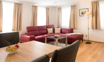 A modern living room with a red sofa and a table. Bright curtains let in a lot of light.