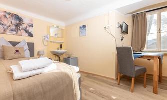 A cozy room with a double bed and a desk. The walls are painted in light colors, and there is a window with natural light.