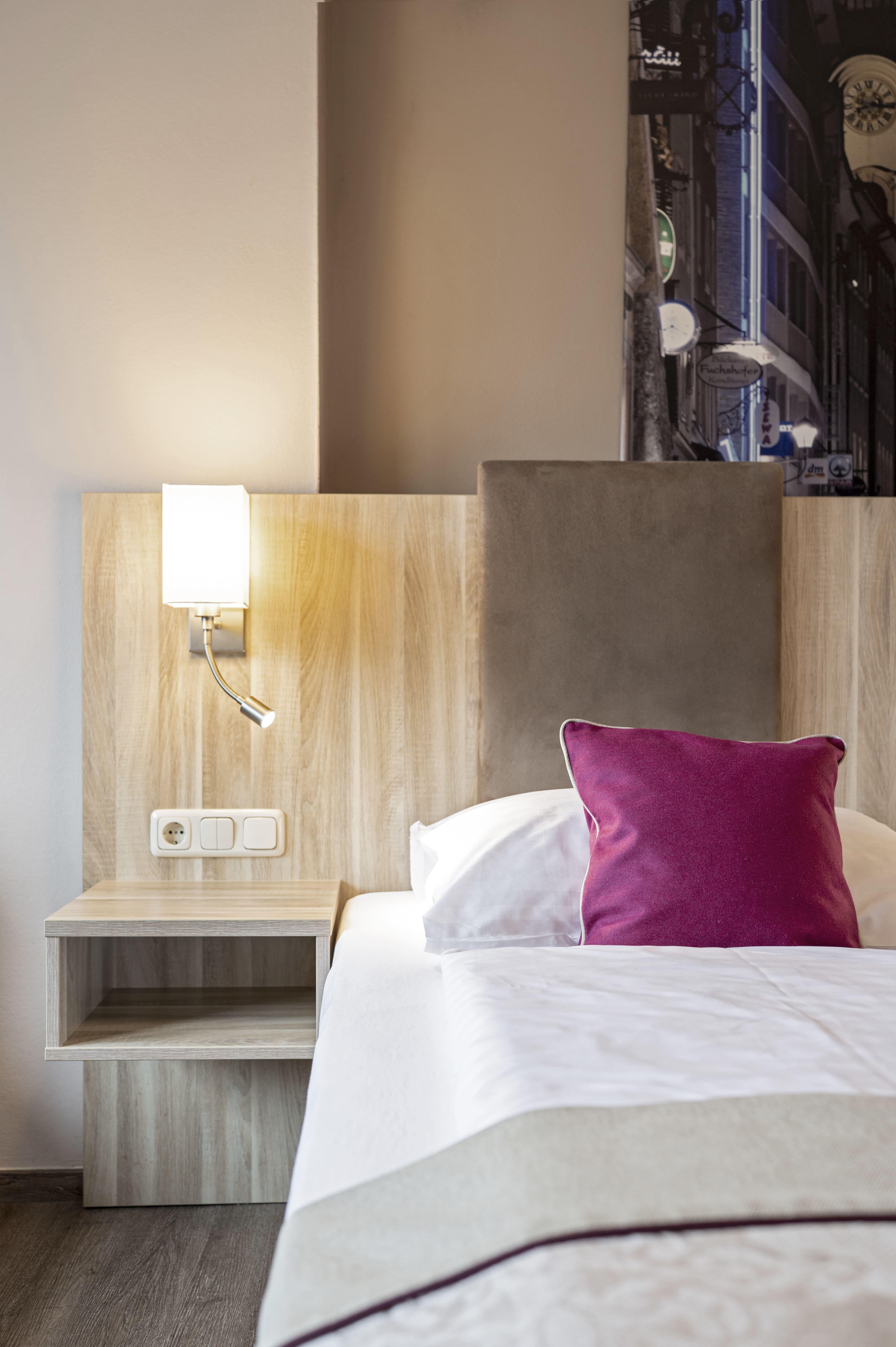 A stylish bedroom with a modern bed and a wooden nightstand. The bright lighting creates an inviting atmosphere.