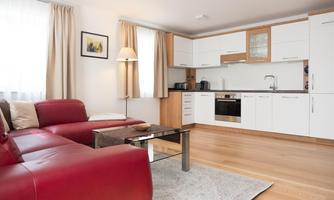 A modern apartment with a red couch and a bright, open kitchen. The room is flooded with light and furnished cozy.