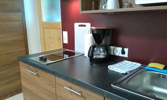 A modern kitchenette with wooden cabinets and a black countertop. On the countertop are a coffee machine and a dish towel.