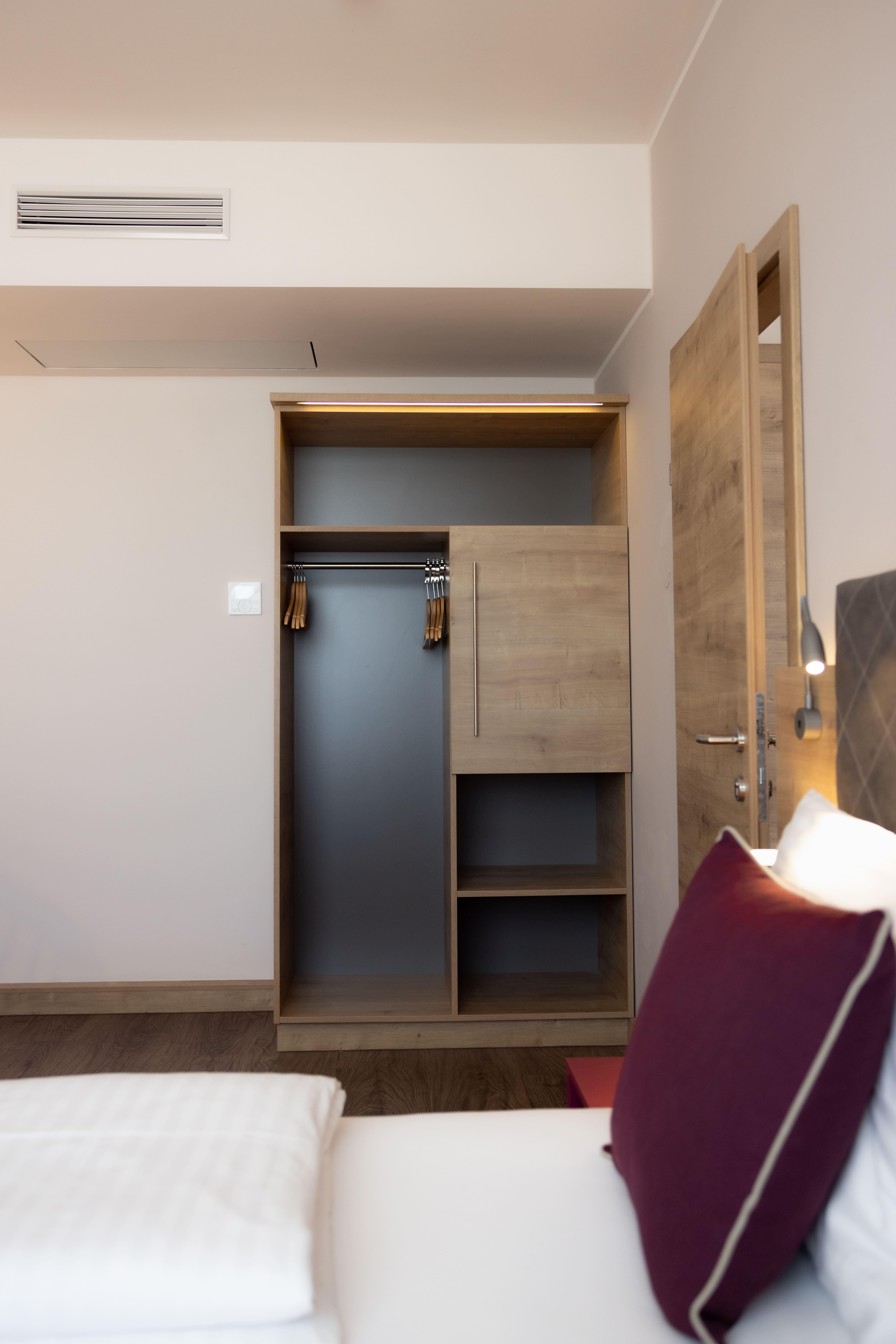 A modern room with a wooden wardrobe and a large mirror. The walls are light and the floor is made of wood.