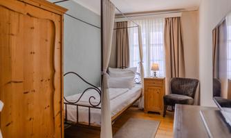 A cozy bedroom with a four-poster bed and a wooden chest. The window lets in plenty of light, and the room has a warm, inviting character.