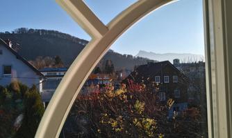 A view from a window of a peaceful urban landscape. In the background, mountains and a clear sky can be seen.