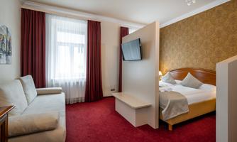 A cozy hotel room with a double bed and a sofa. The walls are decorated with red carpet and elegant curtains.