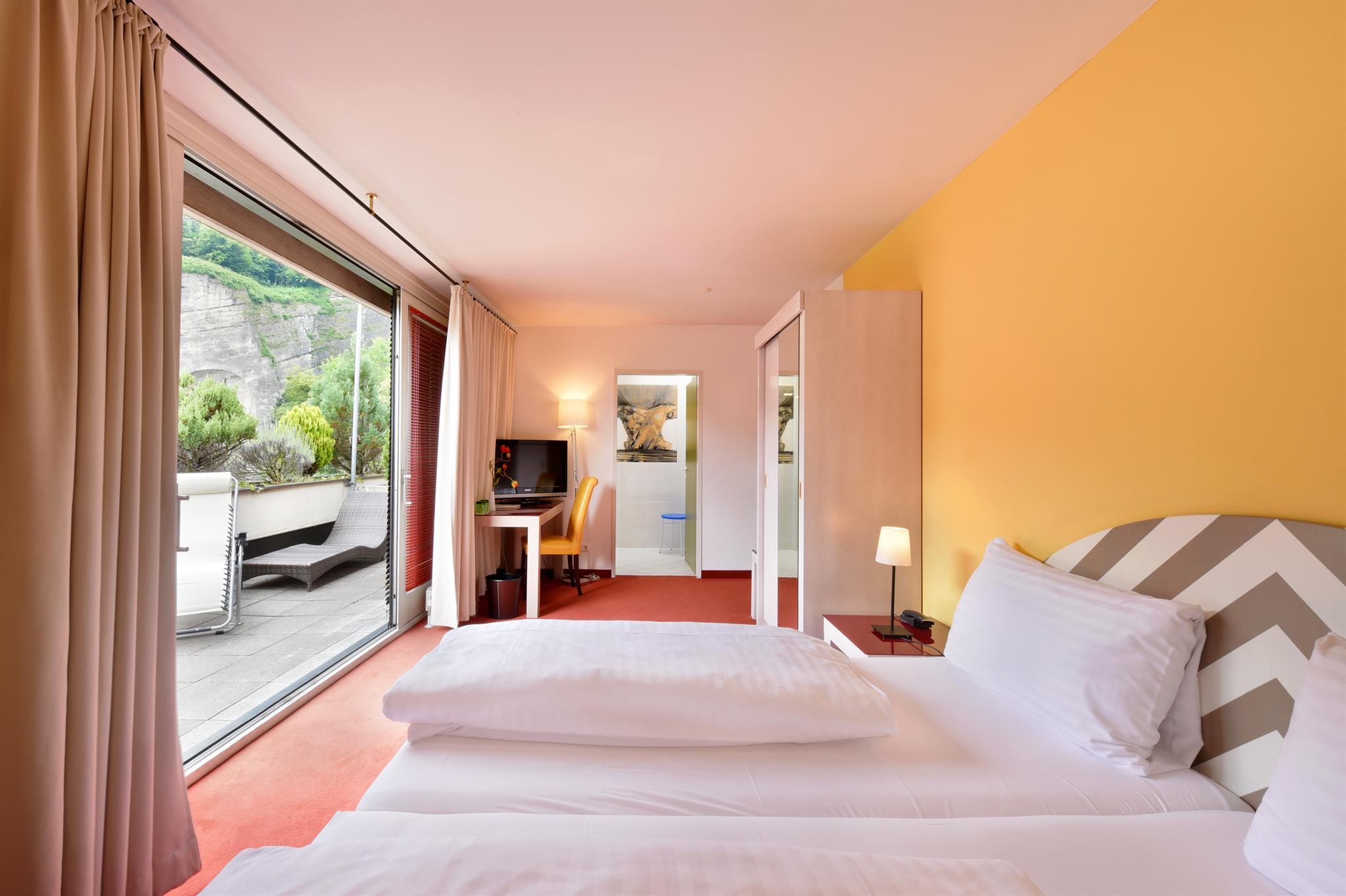 A modern hotel room with a large window and access to an outdoor area. The walls are painted in warm colors, and the room is stylishly furnished.