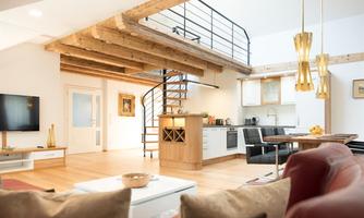 A modern apartment with light walls and an open kitchen. An elegant staircase leads to the upper area of the room.
