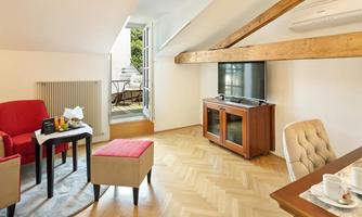A bright, cozy living room with red furniture and wooden beams. A television is situated opposite a seating area with access to a balcony.