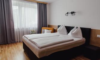 A modern bedroom with a double bed and white bedcovers. Large windows let in plenty of daylight.