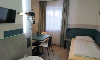 A modern room with a table, chairs, and a large window. There is a television on the wall and a bed with fresh linens.