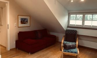 A cozy room in the attic with a red sofa and a blue chair. The windows provide pleasant daylight.