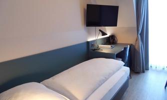 A modern bedroom with a single bed, a desk, and a television.  
Large windows let in plenty of light and create a pleasant atmosphere.
