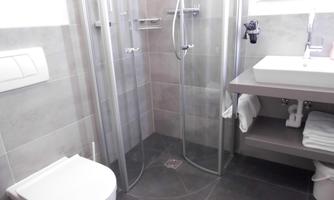 A modern bathroom with a glass shower and an elegant sink. The room is decorated in neutral colors and appears bright and clean.
