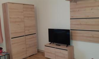 A simple room with modern wooden-look furniture. There is a television on a dresser and a wardrobe against the wall.