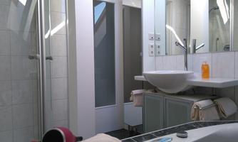 A modern bathroom with a shower and a sink. The walls are brightly tiled and a large window lets in plenty of light.