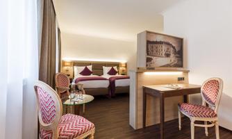 A modern hotel room with two beds, a small table, and elegant chairs. Generous light flows through the window, creating an inviting atmosphere.