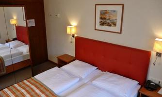 A cozy hotel room with a double bed and an orange headboard. A mirrored wall and warm lighting create an inviting atmosphere.