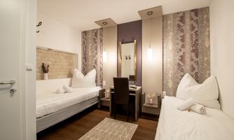 A cozy room with two single beds and an elegant table. The walls are stylishly decorated, and there is pleasant lighting.