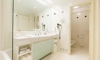 A modern bathroom with a double sink and large mirrors. The walls are light-tiled and there are towels on a shelf.