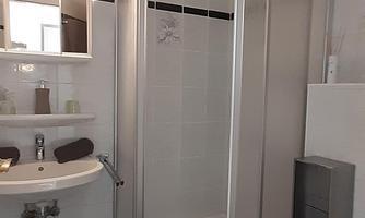 A modern bathroom with a shower stall, a sink, and a toilet. The floor is covered with black tiles.