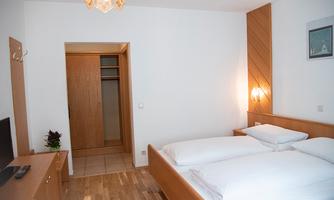 A simple bedroom with two single beds and a wardrobe. The room has a bright floor and a cozy atmosphere.