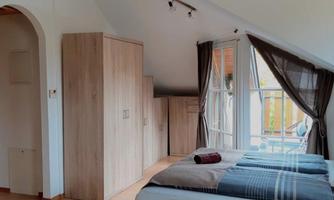 A bright bedroom with two beds and large windows. The room is simply furnished and has a modern, minimalist style.