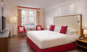 A modern hotel room with a large bed and red accents. Next to the bed are two cozy chairs and a table.
