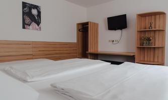 A simple room with two beds and white bed covers. 

On the wall, there is a picture, and there is a television as well as a small table.