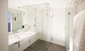 A modern bathroom with a glass shower and an elegant sink. The walls are bright, and the lighting creates a pleasant atmosphere.