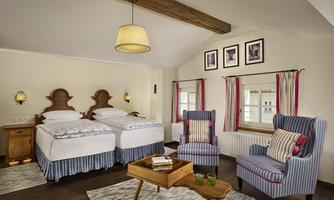 A cozy room with two single beds and comfortable armchairs. Large windows provide plenty of daylight and an inviting atmosphere.
