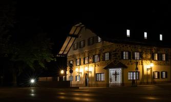 A charming building at night, illuminated by warm light. In the foreground, trees and streetlights can be seen.