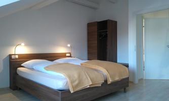 A simple bedroom with a double bed and two bedside lamps. There is a wardrobe and a bright, friendly room.