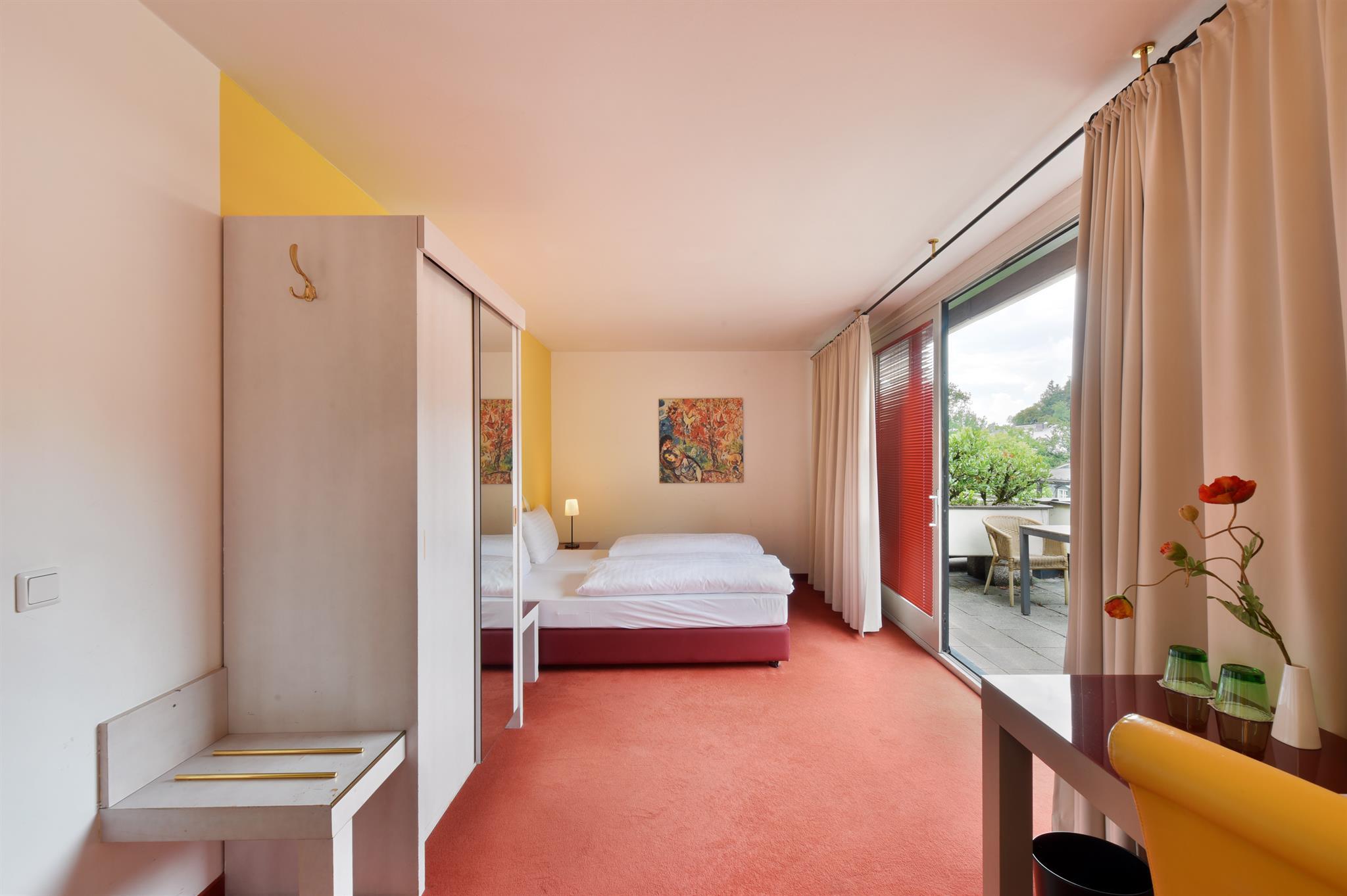 A modern room with a large window and access to the terrace. The floor is red and the walls are brightly designed.