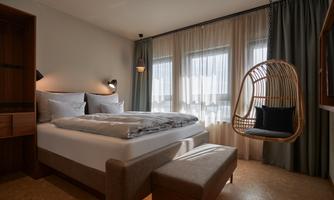 A modern bedroom with a cozy bed and a hanging swing. Large windows provide plenty of natural light.