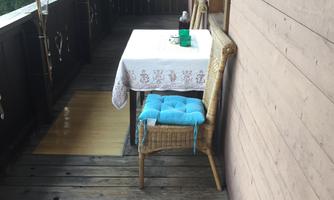 A cozy balcony with a table and a chair. The table is set with a white tablecloth and a bottle of water.