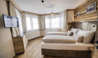 A modern bedroom with wooden details and two beds. Large windows ensure bright light entry and a cozy atmosphere.