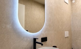 A modern bathroom with an elegant, oval mirror light. The sink is simple, round, and generous. There is plenty of space in the drawer under the sink.